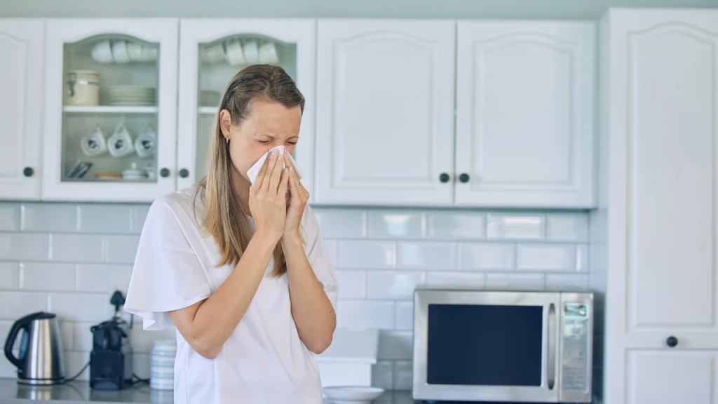 Woman sneezing due to poor indoor air quality caused by dirty air ducts.