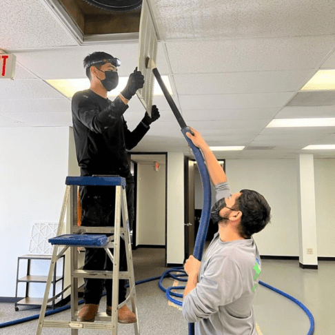 Air Duct Cleaning - Two technicians work on a ceiling fan in an office, surrounded by air duct cleaning tools working on air duct mold removal